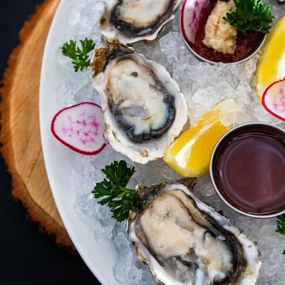 Close up of a plate of oysters on ice with lemon, radish slices, and dipping sauces