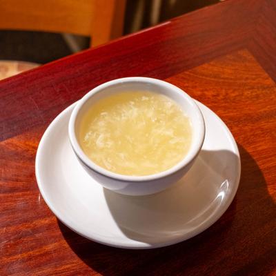 Egg flower soup in a white bowl placed on a white plate on a wooden table.