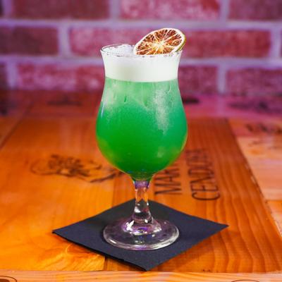 Vibrant green cocktail topped with thick foam and garnished with a dry citrus wheel.