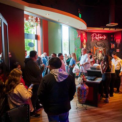 A lively restaurant scene with people gathered near a vibrant mural and neon sign.