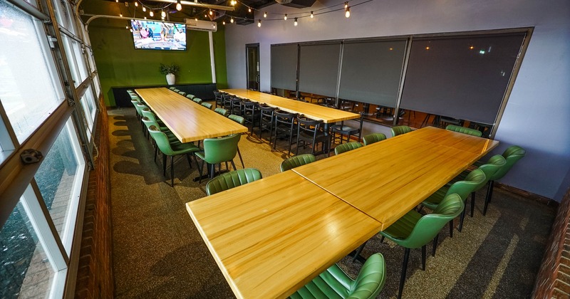 A spacious room with long wooden tables and green chairs arranged in rows