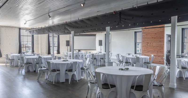 Interior, event space, white cloth round tables, white brick walls, presentation panel