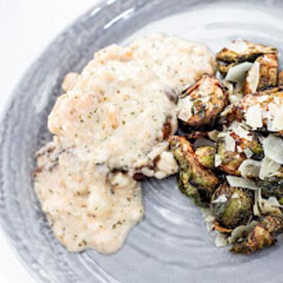 Plated dish features creamy chicken breast in white sauce and roasted Brussels sprouts.