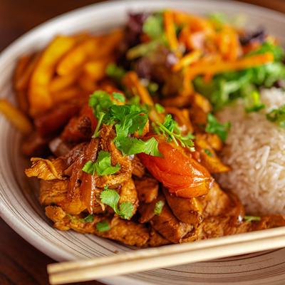 Stir fry chicken with vegetables served over a bed of fries, with side of rice