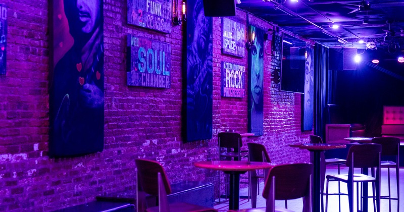 A bar interior with exposed brick walls, purple lighting, and music-themed posters