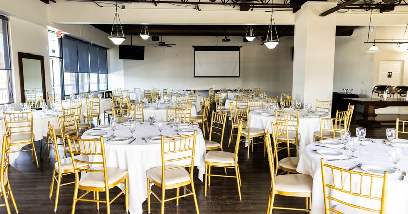 Interior, banquet hall set for an event, round tables, tablecloths, gold chairs, projector screen