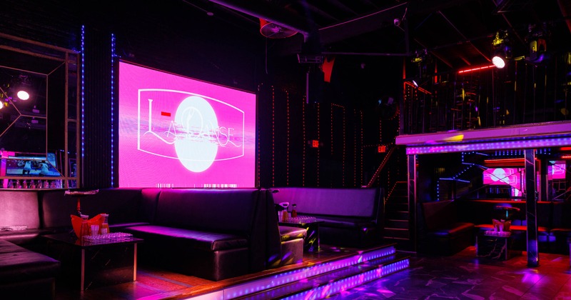 Nightclub interior with couches, colorful lighting and a large illuminated screen.