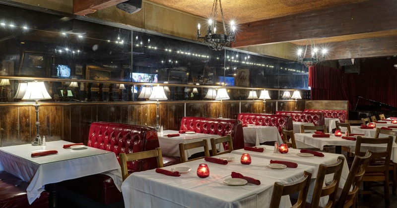 A cozy interior - red leather booths, wooden tables with white tablecloths and ambient lighting