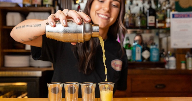 A bartender pouring a drink into glasses