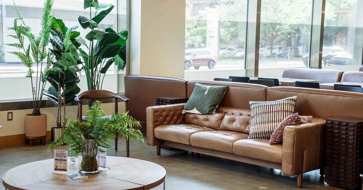 A modern lounge area featuring a round wooden coffee table, a brown leather couch and pillows