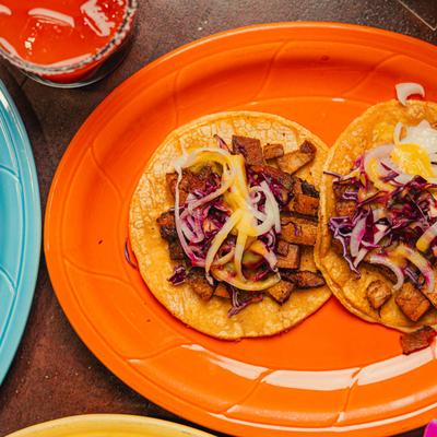 Pork belly taco order on an orange platter with a drink.