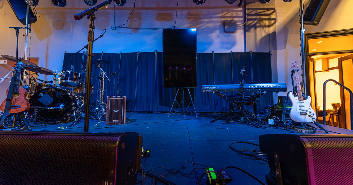 Stage setup with musical instruments and equipment, including drums, guitars, a keyboard, speakers, and stage lights.