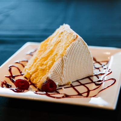 Lemon cake slice with berry sauce drizzle and raspberry garnish.