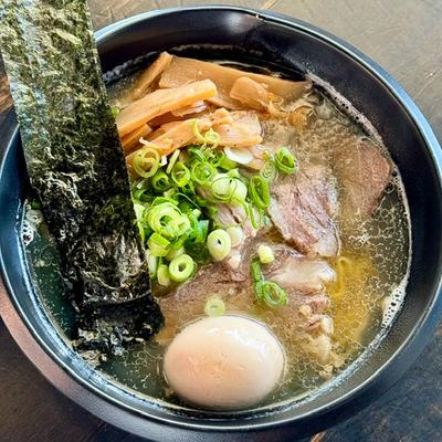 A bowl of ramen with slices of pork, a boiled egg, green onions, bamboo shoots, and seaweed.