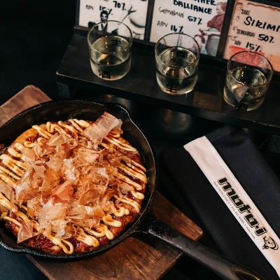 Okonomiyaki served in a skillet, alongside a sake flight.