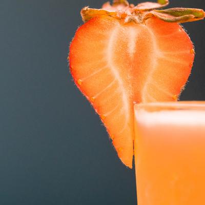 Extreme close up of a glass of a red beverage garnished with a strawberry.