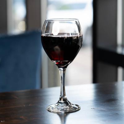 A glass of red wine sits on a wooden table, warmly lit by soft natural light from a window.