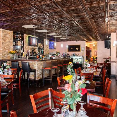 A room with a bar and dining area with glassware and floral arrangements on tables.