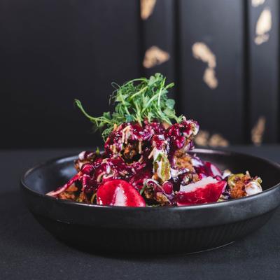 Bowl of vibrant food with reddish-purple sauce and green garnish against a dark background.
