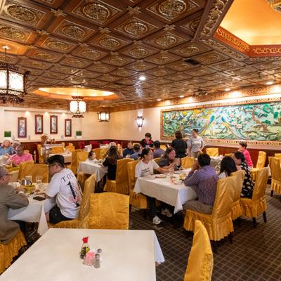 Interior featuring ornate ceilings, yellow chairs and people seated at tables.