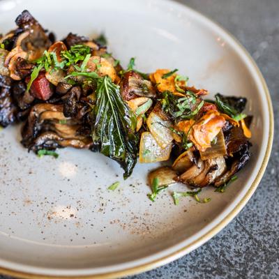 dish of mushrooms and bacon lardons with fried herb leaves on taupe plate