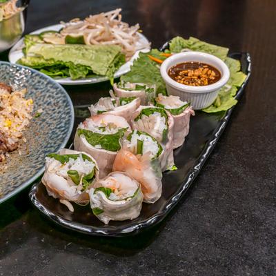 Avocado spring rolls served with a dipping sauce on a dark rectangular plate..