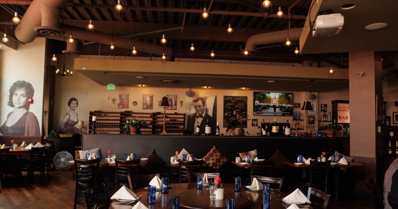 Cozy restaurant interior with wooden floors, round tables set with blue glassware, and black chairs