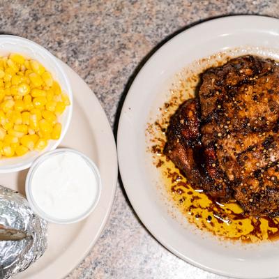 Steak served with corn, sour cream, and a baked potato wrapped in foil.
