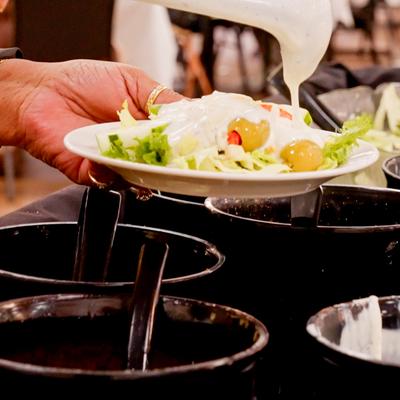 Person serving themselves food with a white dressing being poured over it.