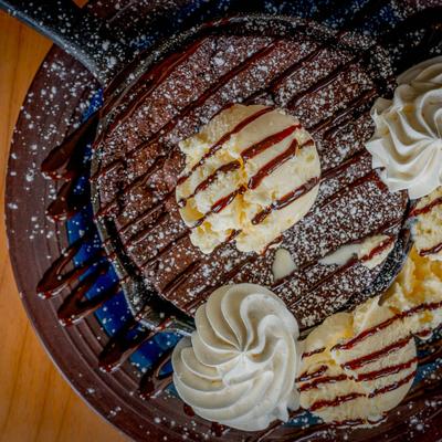 Brownie topped with ice cream and whipped cream, served in a small skillet.