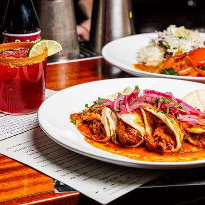 Plate of tacos served on the table with menus, a cocktail and a shrimp dish.