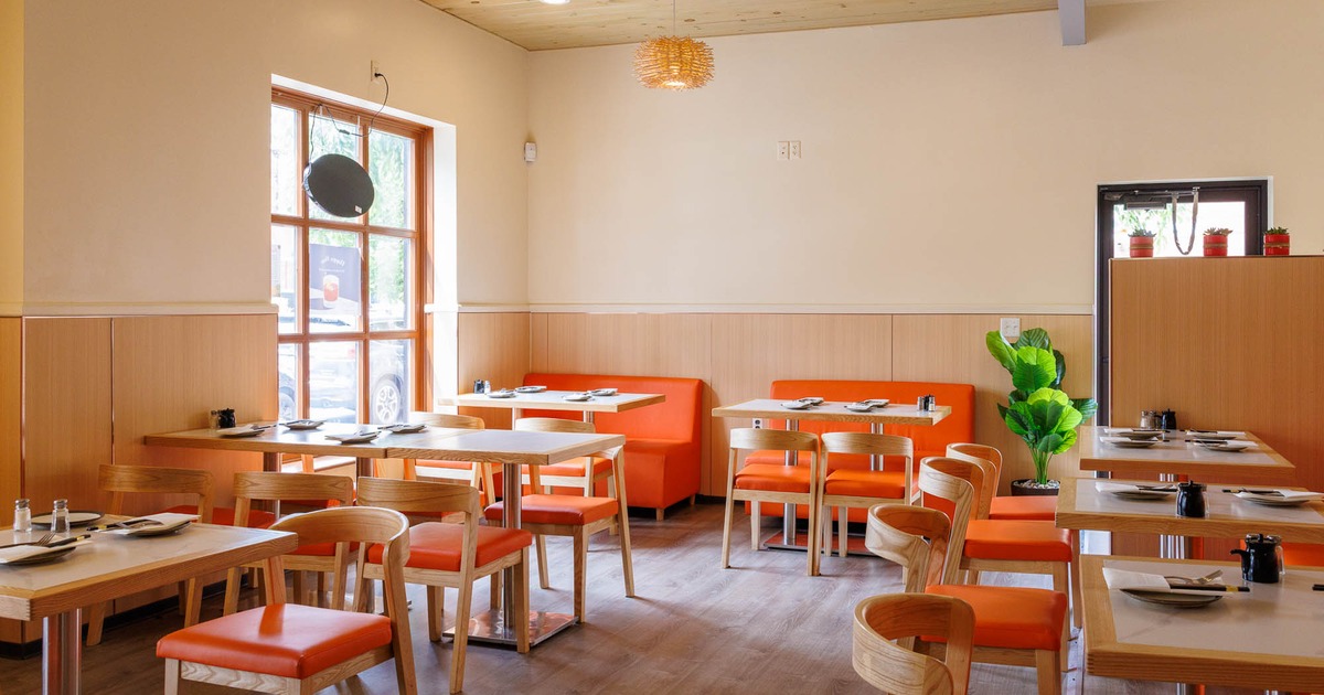 Modern restaurant interior with wooden tables, orange seating, and natural light.
