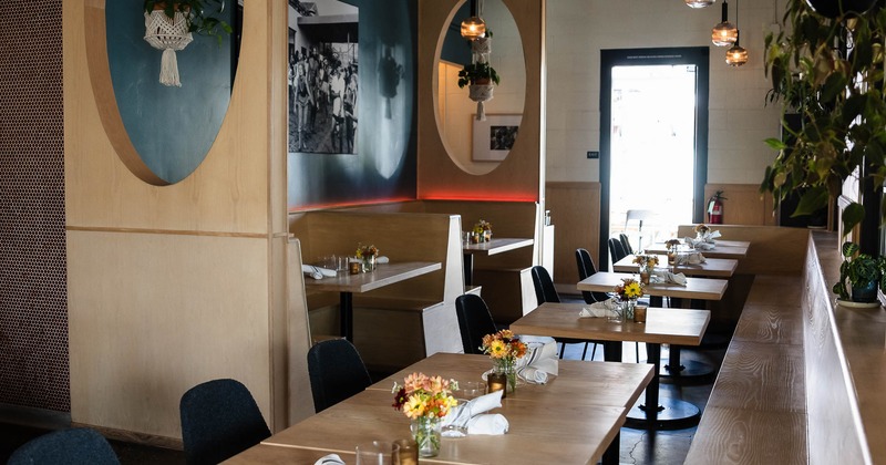 Modern restaurant interior with light wooden tables, black chairs and decorative lighting