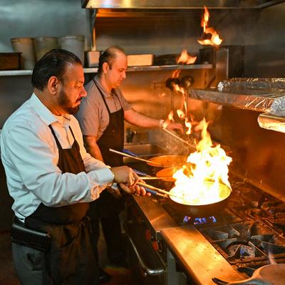 The staff cooking with an open flame in pans.
