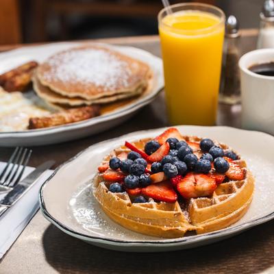 Waffles with fresh berries, pancakes, eggs, and sausage, with orange juice and coffee.