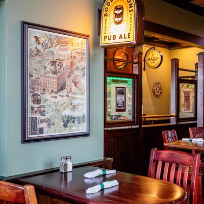 Pub dining area featuring wooden tables with rolled napkins and framed vintage artwork.