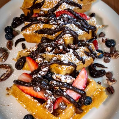 Waffles topped with chocolate drizzle, berries, powdered sugar, and chocolate chips.