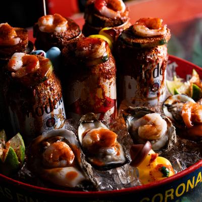 Party platter featuring iced canned beers, spicy cooked shrimp and fresh oysters.