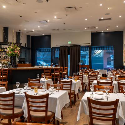 Restaurant interior with set dining table, bar seating, and curtained entrance.
