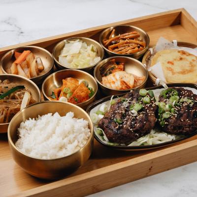 Tteokgalbi platter featuring sides of rice, noodles and various condiments.