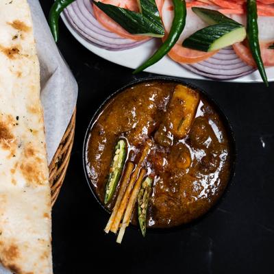 Curry bowl with a plate of sliced vegetables and a basket of naan.