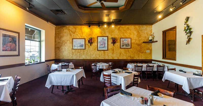 Interior, tables with tablecloth, tableware and chairs, walls decorated with pictures
