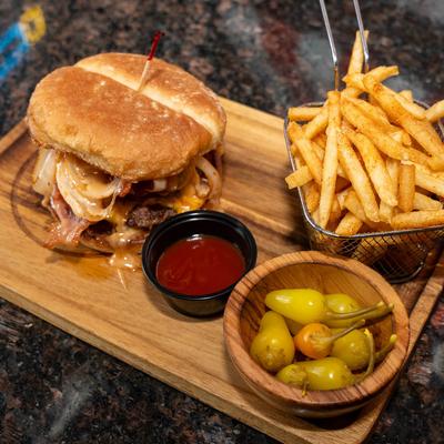 Bacon cheeseburger with fries, pickled peppers, and dipping sauce on a wooden board.