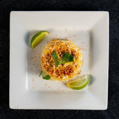 Esquite with mayo, cotija cheese and Tajin, served with lime wedges.