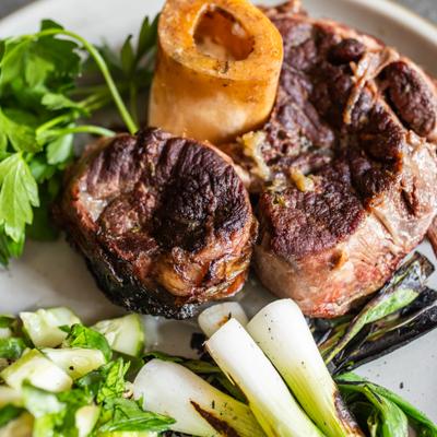 plate showing beef shank, grilled scallions and fresh herbs