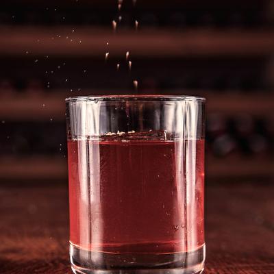 Cocktail in a rocks glass with small particles falling into it.