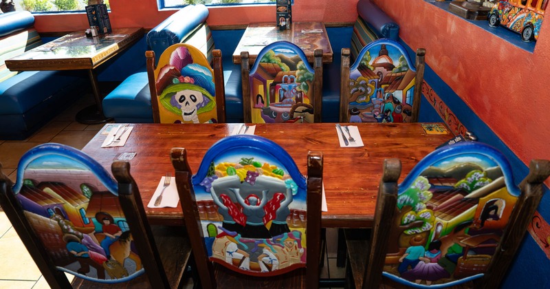 Interior, wooden dining chairs with vibrant, colorful Mexican folk art surround a wooden table