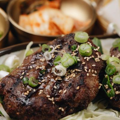 Grilled short rib patties topped with green onion and sesame seeds, close-up.