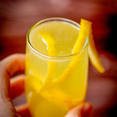 A hand holding a mimosa garnished with a lemon twist.