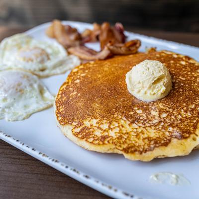 Pancakes tipped with butter, with two fried eggs and strips of bacon.